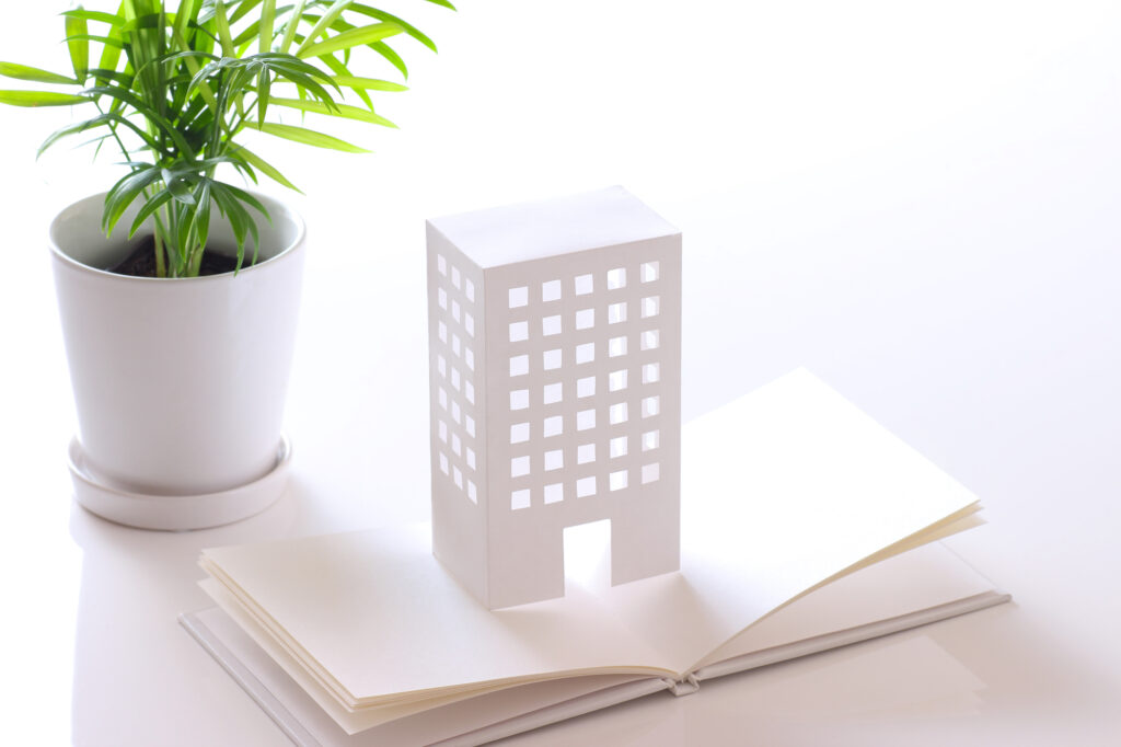 本の上に乗っている白いビルの模型、後ろに植木鉢
